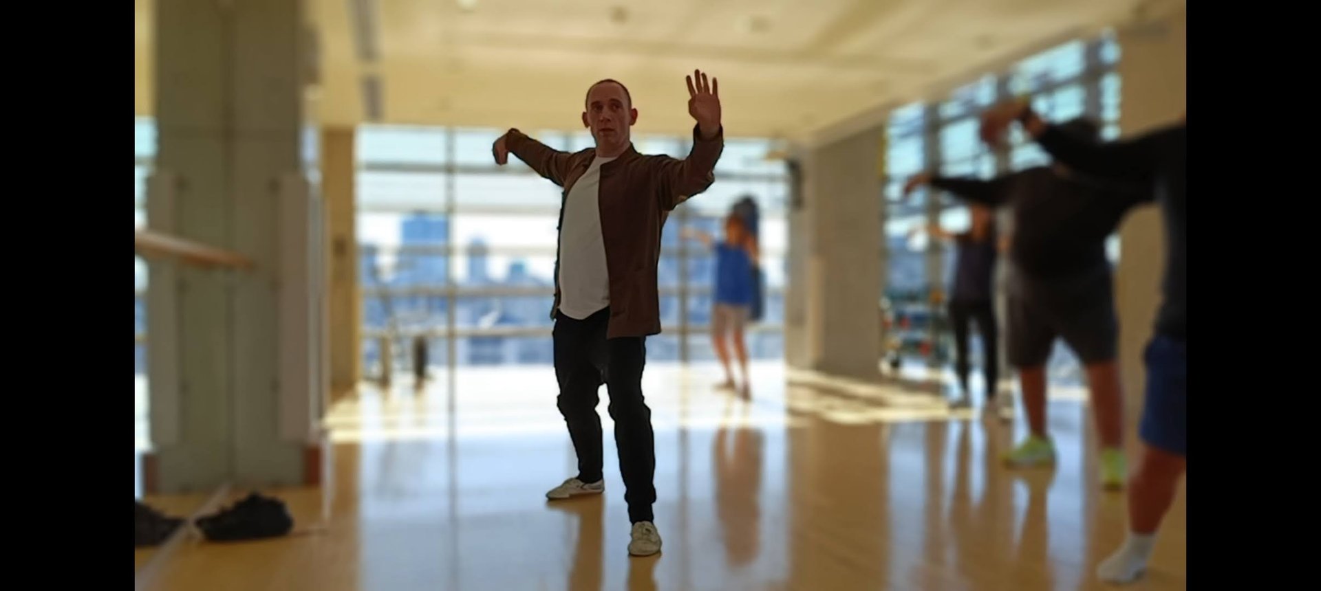 A man practices Tai Chi movements during a martial arts class in a bright fitness studio.