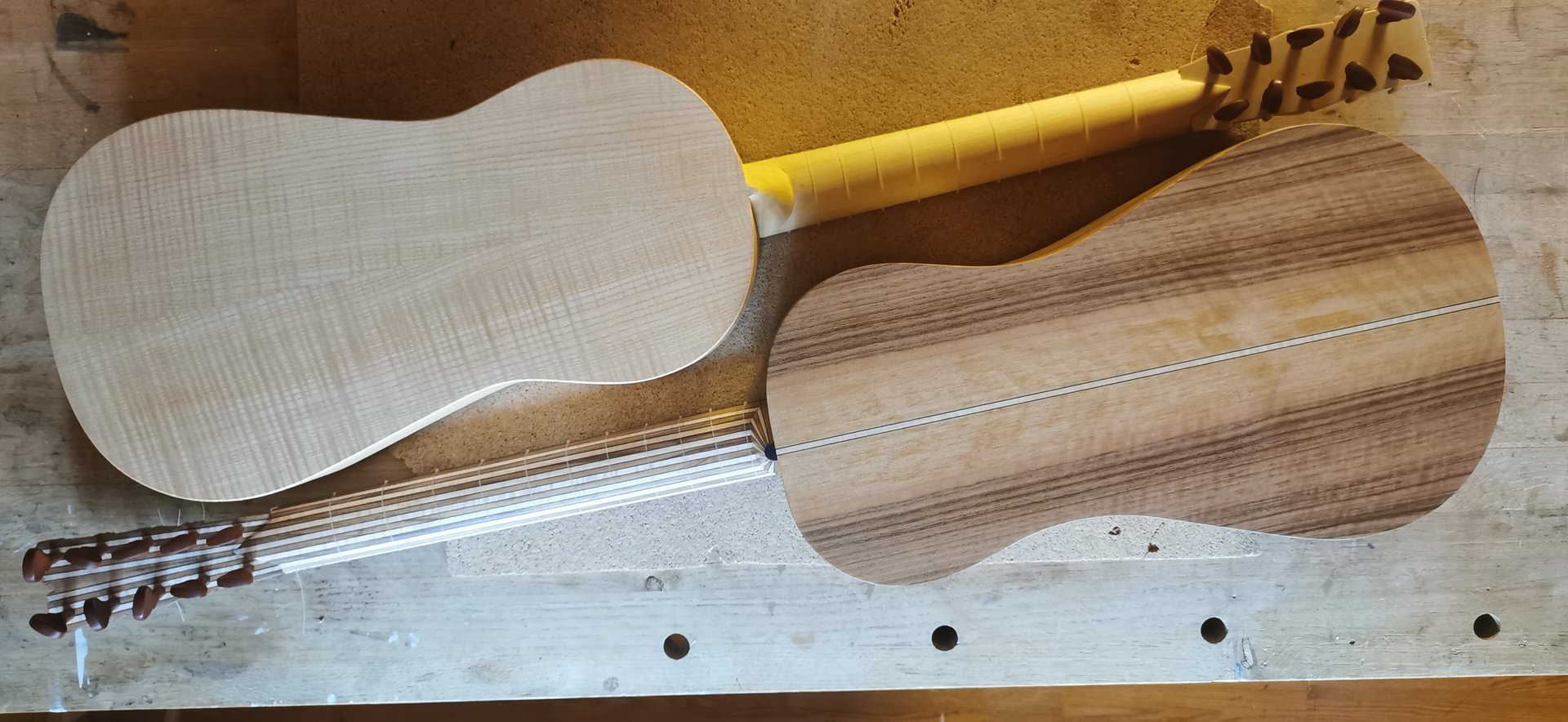 Two handmade baroque guitars in progress showing flamed maple and walnut wood grain on a workbench.
