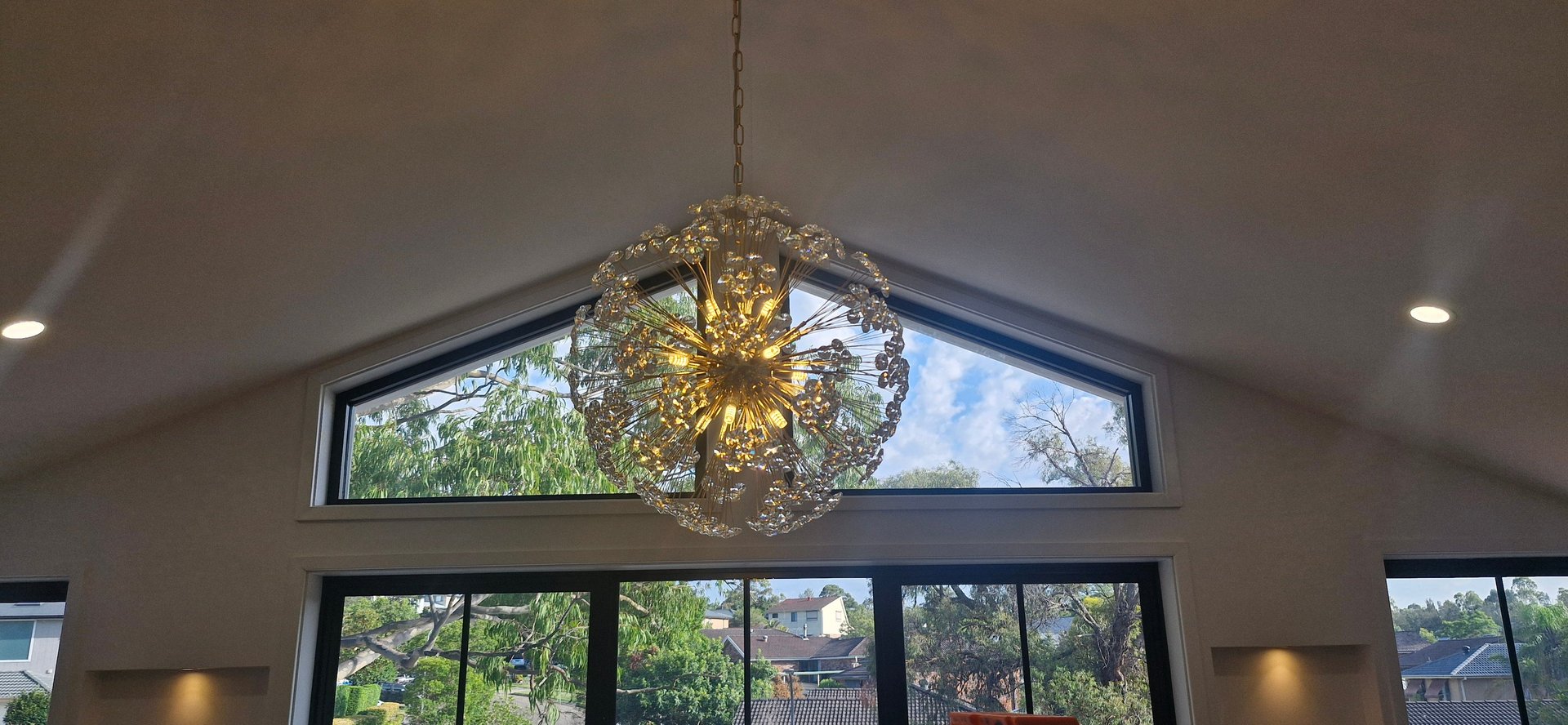 Elegant crystal sputnik chandelier hanging from a vaulted ceiling in a modern home with large windows.