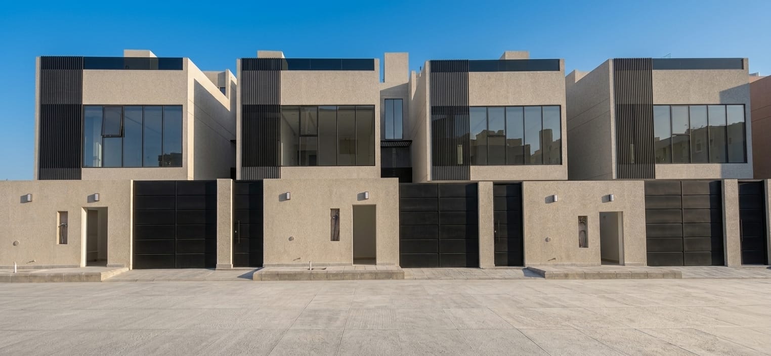 Modern luxury townhouses with minimalist concrete architecture and large glass windows under a clear sky.