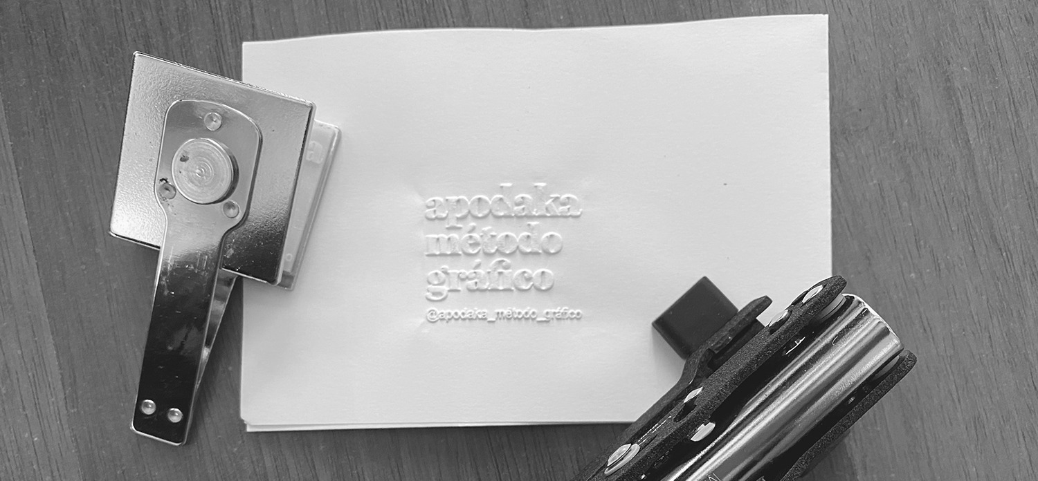 Sello metálico estampando en relieve el logotipo 'apodaka método gráfico' sobre papel blanco