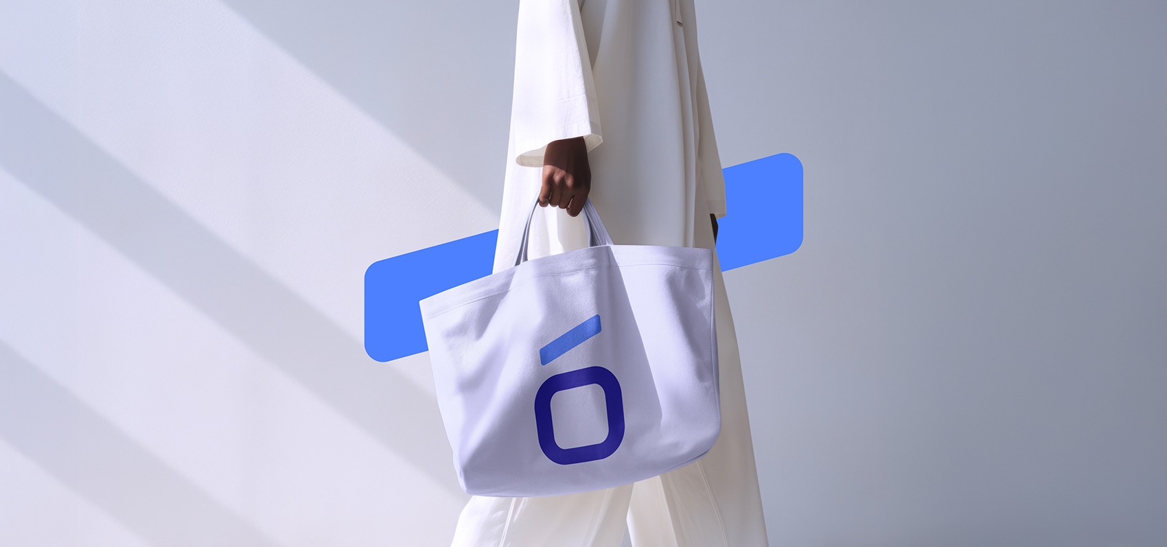 A person in white clothing carrying a large white branded tote bag with a blue logo.