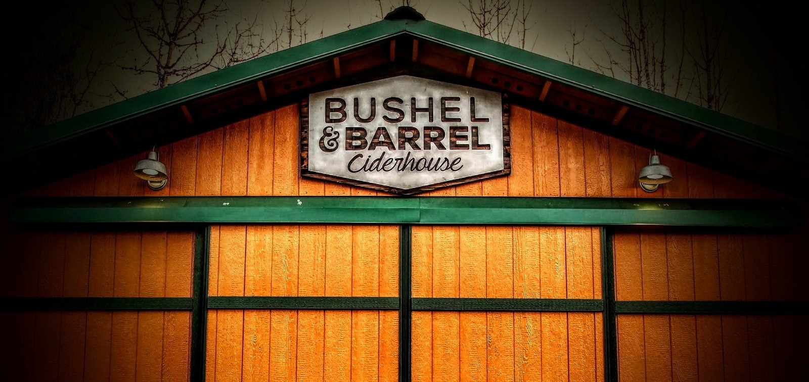Rustic wood exterior of Bushel & Barrel Ciderhouse with a branded sign and green trim.