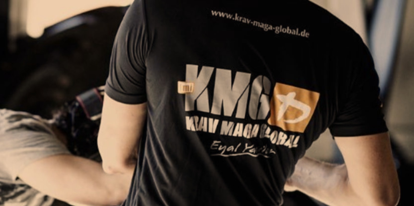 KMG Krav Maga Global instructor wearing a branded black t-shirt during a self-defense training session.