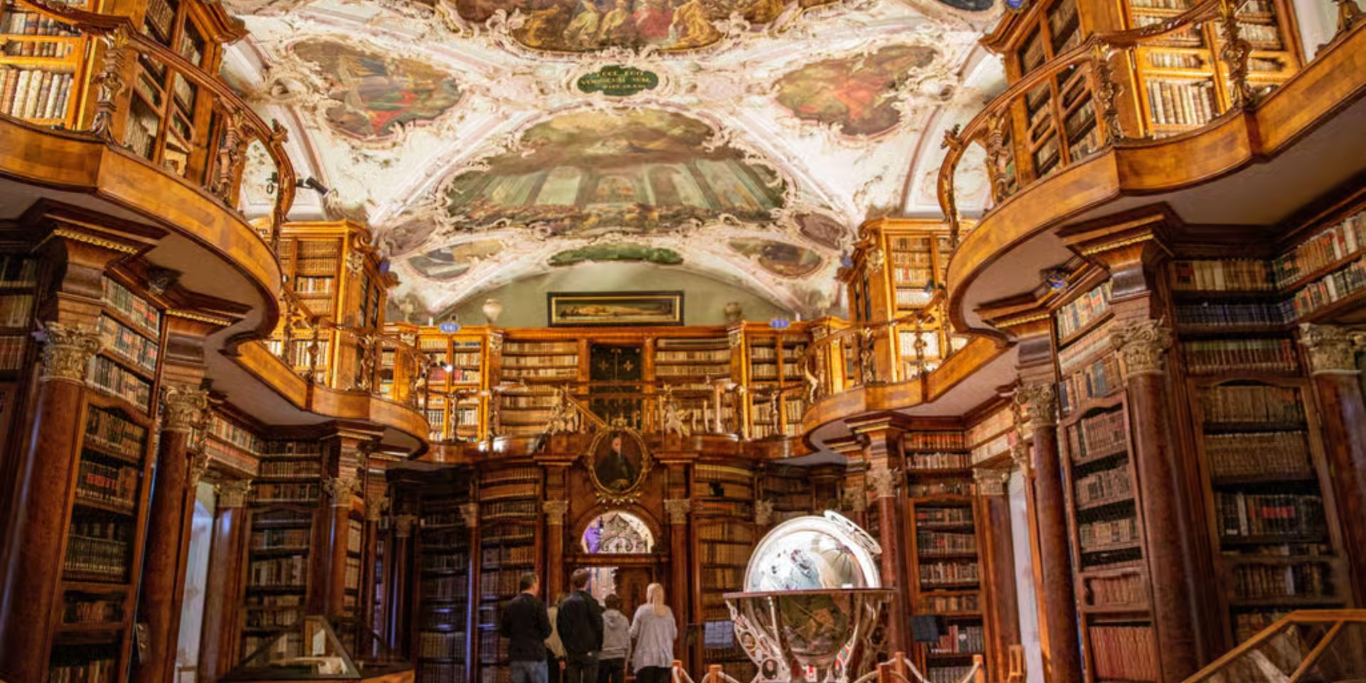 Ornate baroque interior of the Abbey Library of Saint Gall featuring ceiling frescoes and wooden bookshelves.