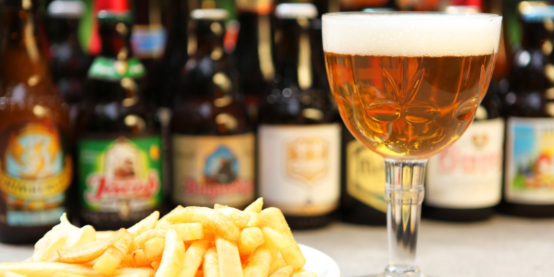 A glass of Belgian craft beer served with golden french fries and bottled beers in the background.