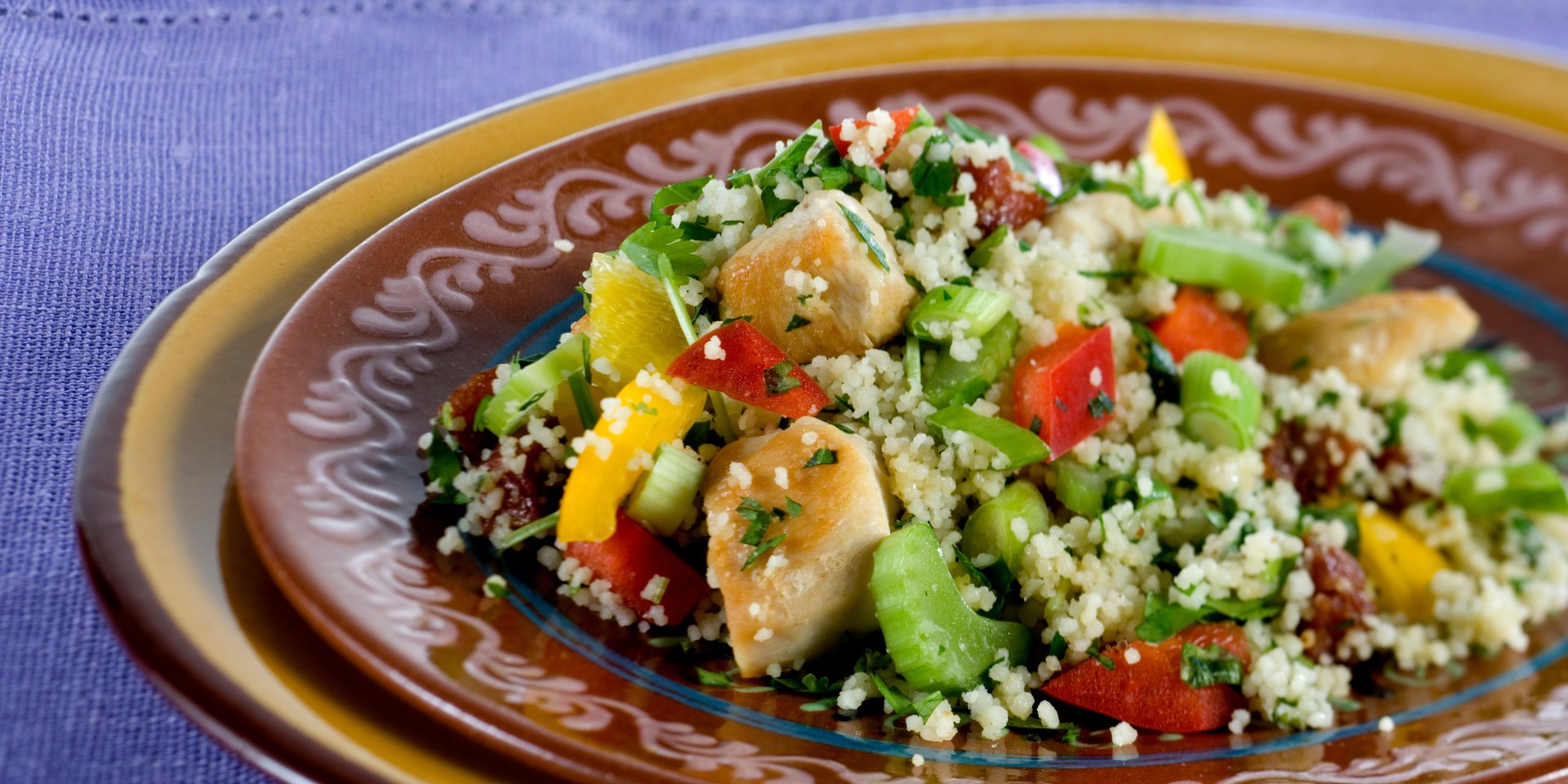 A healthy chicken couscous salad with bell peppers and celery on a brown ceramic plate.