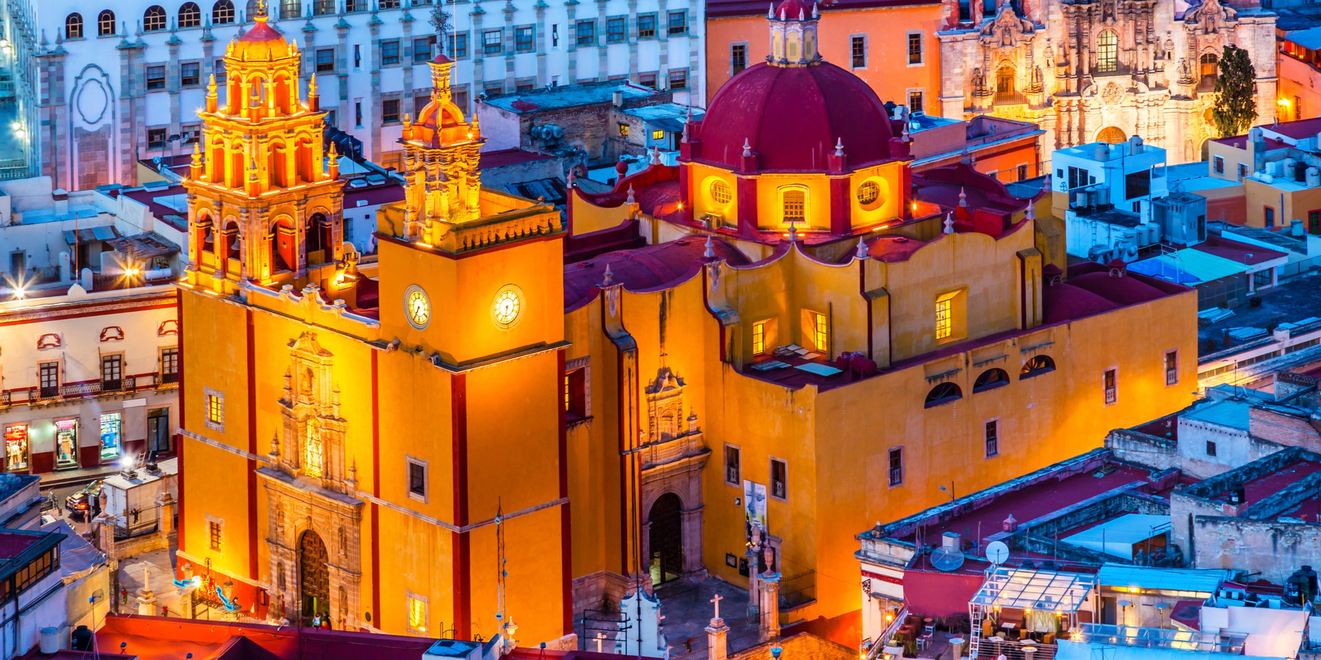 Illuminated yellow facade and red dome of Basilica of Our Lady of Guanajuato at twilight in Mexico.