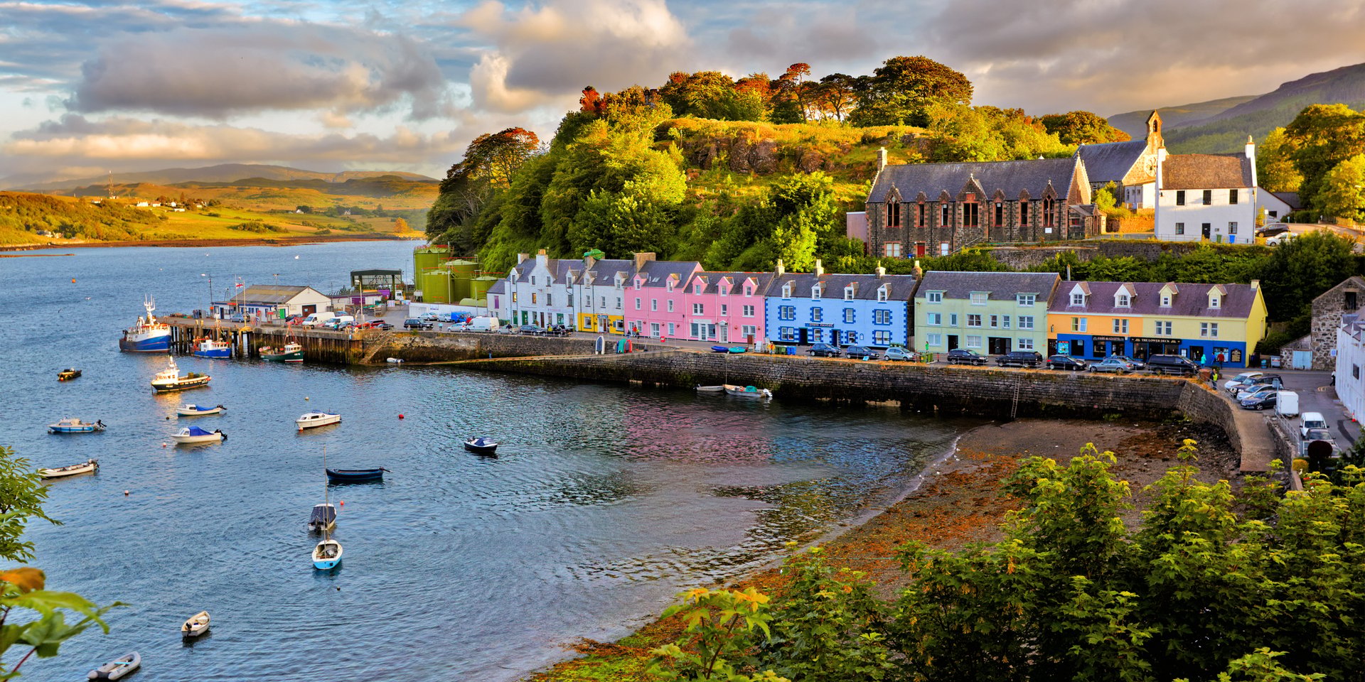 Colorful coastal houses and fishing boats in Portree harbor on the Isle of Skye, Scotland at sunset.