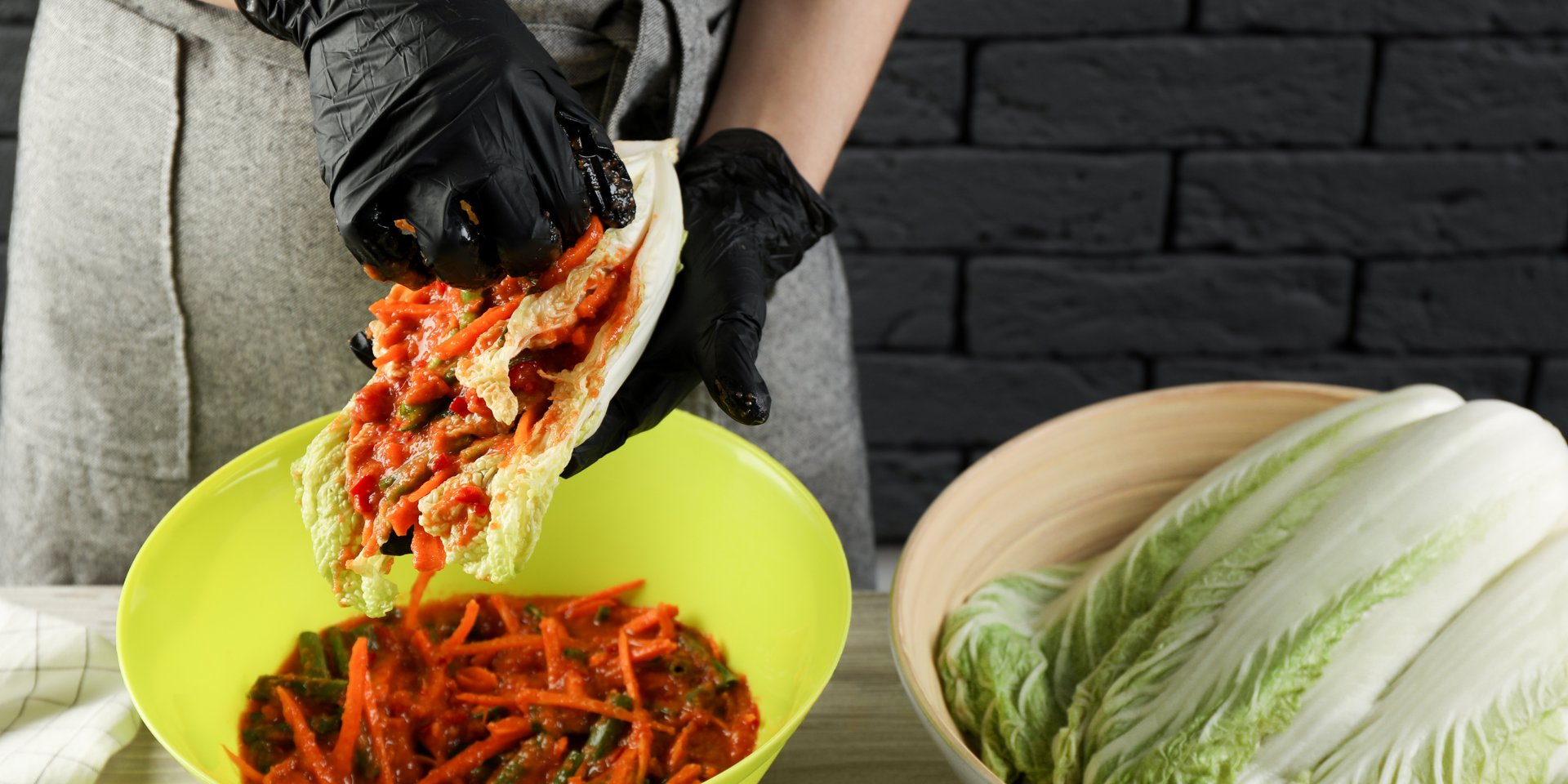 Chef in black gloves preparing authentic spicy Korean kimchi with napa cabbage and red pepper paste.