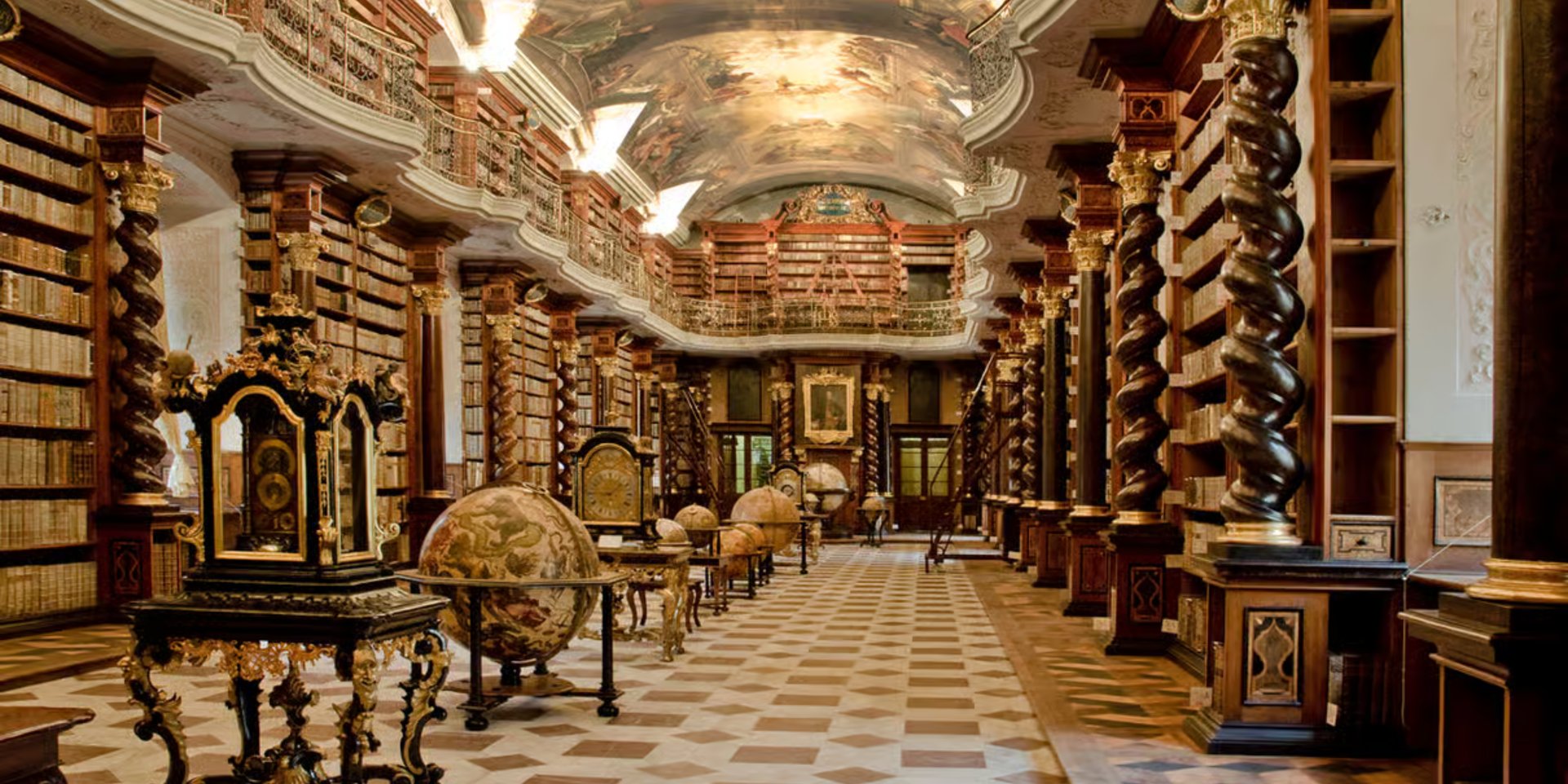 Baroque library hall with ornate wooden shelves, globes, and a frescoed ceiling.