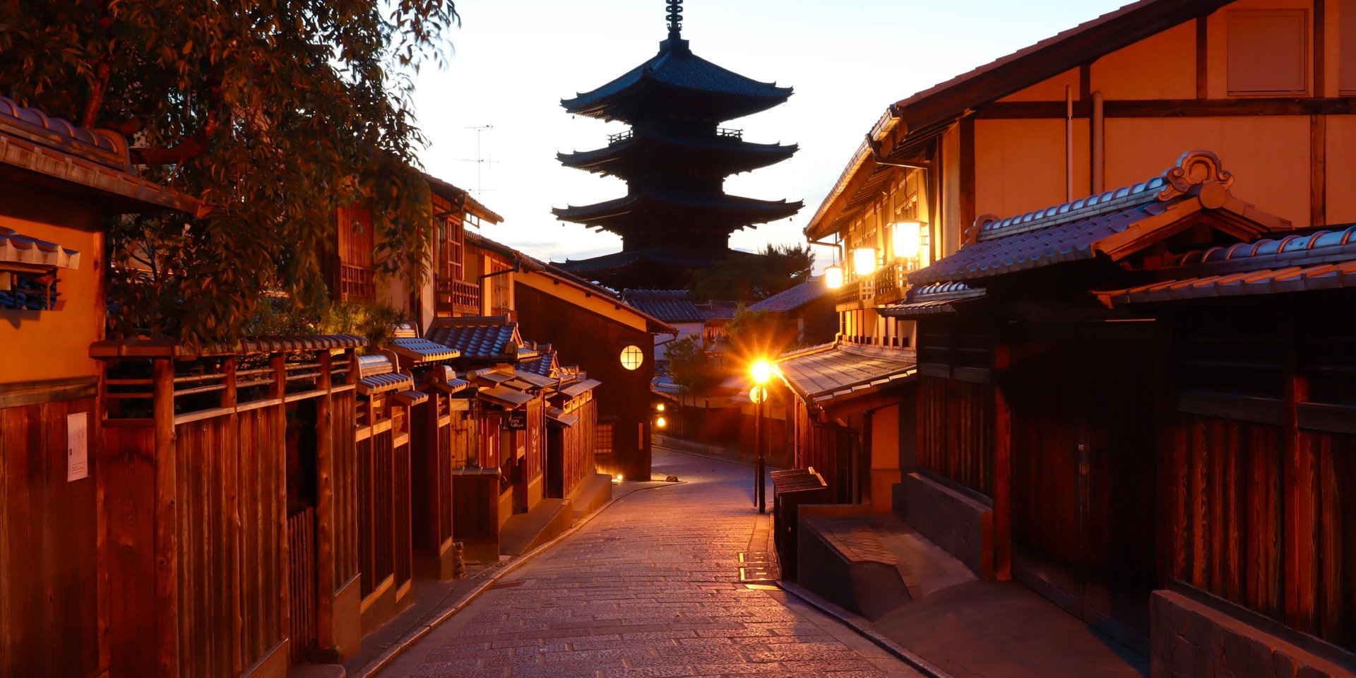 A sunset view of a historic Kyoto street leading toward the Yasaka Pagoda with traditional wooden buildings.