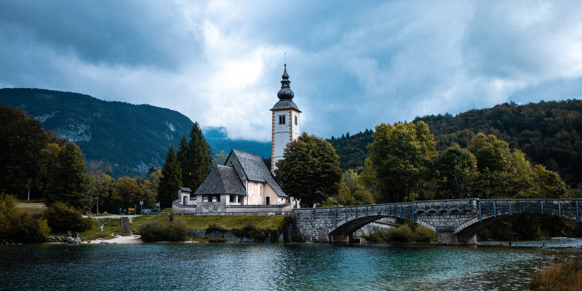 Church of St. John the Baptist and stone bridge on Lake Bohinj, Slovenia, with mountain landscape.