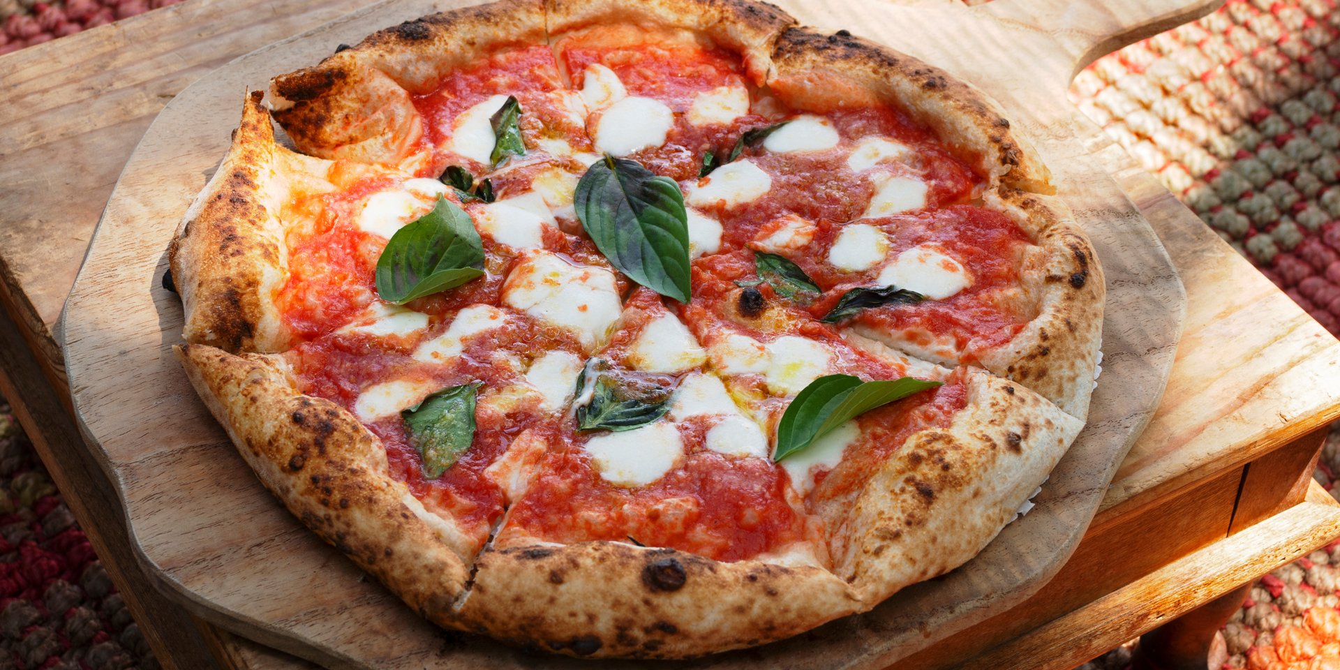 Wood-fired Neapolitan pizza Margherita with fresh buffalo mozzarella, tomato sauce, and basil leaves on a wooden peel.