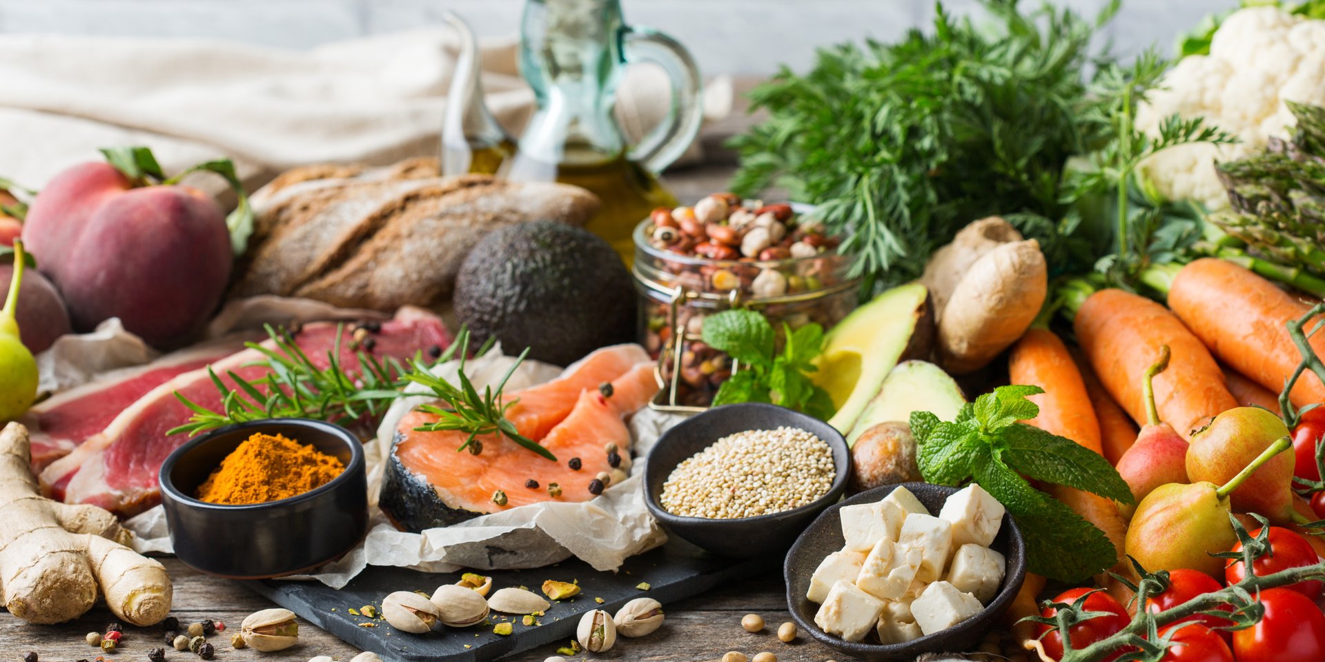 Fresh healthy Mediterranean diet food ingredients including salmon, avocado, vegetables, and nuts on a wooden table.
