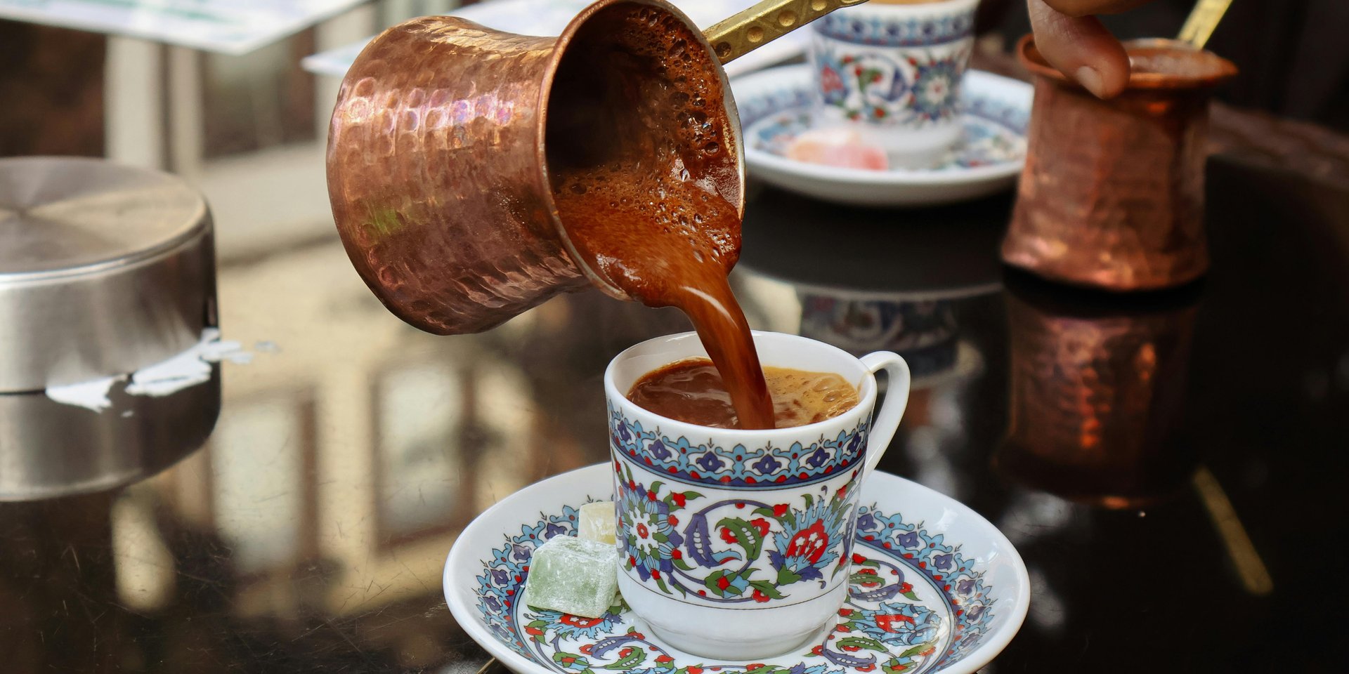 Traditional Turkish coffee being poured from a copper cezve into an ornate ceramic cup.