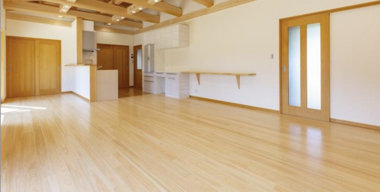 Empty modern open concept living room featuring light hinoki flooring and exposed ceiling beams.