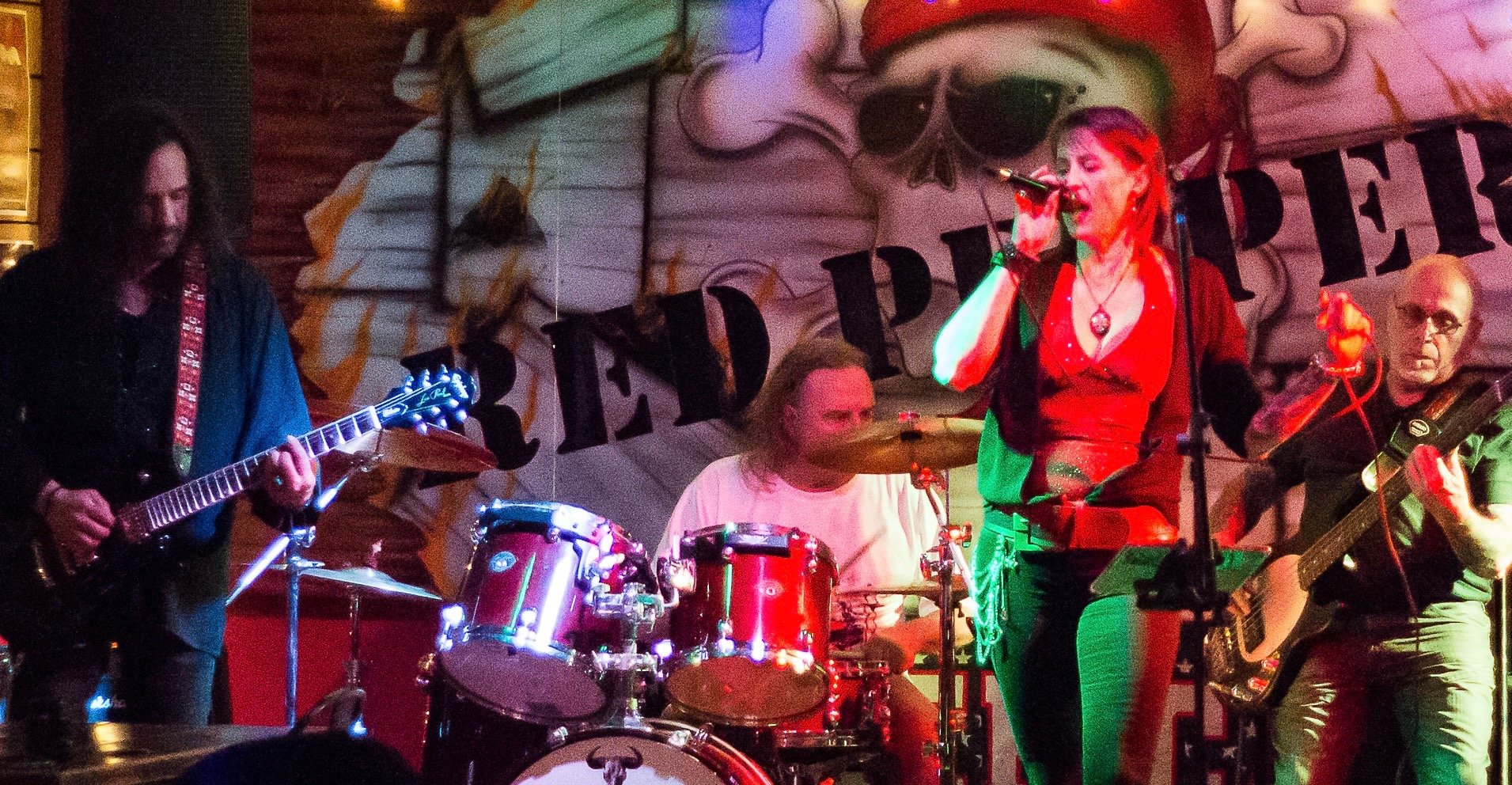 Live rock band performing on stage with female vocalist, guitarist, and drummer at Red Pepper venue.