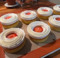 a tray of cupcakes with strawberries and cream