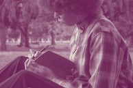 A woman sitting on the ground writing in a book