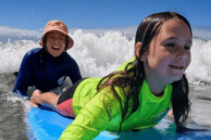 a woman guiding a young girl on a surfboard