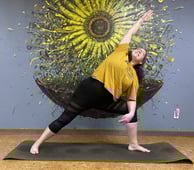 Rachel yoga pose yellow shirt in front of yellow sunflower wall