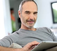 a man sitting on a couch with a tablet computer Martin PE / COACH