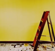 intérieur avec un mur jaune, avec un escabot en bois marron, ave du papier journal au sol 