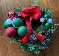 Coroniță de Crăciun cu globuri roșii și verzi, fundă roșie și con de brad, pe fundal din lemn.