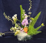 Aranjament floral pentru office cu flori mov, albe și portocalii, pe fundal albastru.