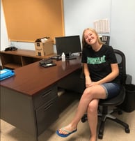 a teacher sitting at a desk with a clock on the wall