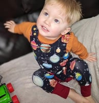 a baby boy wearing a christmas grow with me romper in space bauble fabric