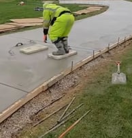 a sidewalk of wet concrete being leveled by a worker that is wearing personal protective gear.