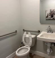 A toilet, sink, and mirror inside the bathroom of a business.