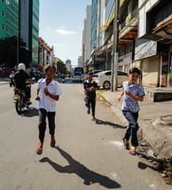Childrens running down a street during a sunny day in Phnom Penh, Cambodia - by ACAT PHOTOS