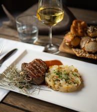 Aufnahme eines Tellers mit einem Steak und Kartoffelbrei sowie ein Glas Weißwein