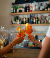 Zwei Gläser stoßen in einer Bar mit einem Aperol-Getränk an