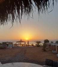 una posta de sol sobre una platja amb una taula i cadires