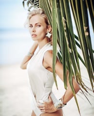 Close-up of a woman in a white bodysuit, large star earrings against a palm leaf background.