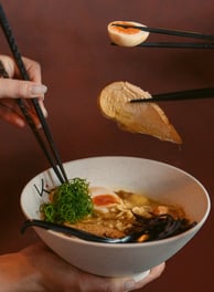 a person holding chopsticks in a bowl of soup