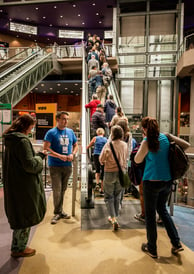 People passing a film festival volunteer and lining up in an escalator leading to a movie theatre