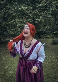 Femme rousse riante et joyeuse dans une robe violette et blanche dans un fond verdoyant