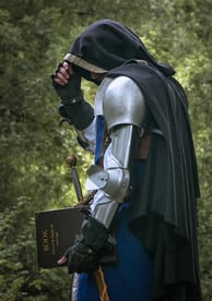 Homme mystérieux en armure et cape sur un fond de feuilles verdoyante. C'est peut-être un rôdeur