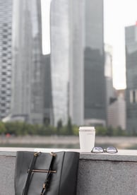 a black tote with a coffee cup on a wall with city buildings in the background