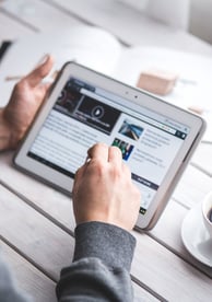 Man using a tablet to read digital news at a desk with a cup of coffee