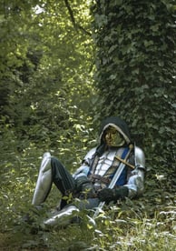 Homme mystérieux en armure et tenue galonnée mystérieusement assis contre un arbre