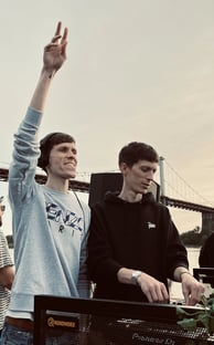 Two dj men standing in front of a large screen