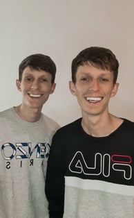 two men standing next to each other in front of a white wall