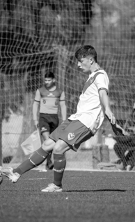 a young man kicking a soccer ball in a soccer field