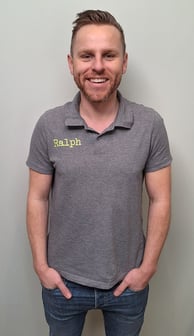 een man in een grijs shirt en broek die voor een muur staat